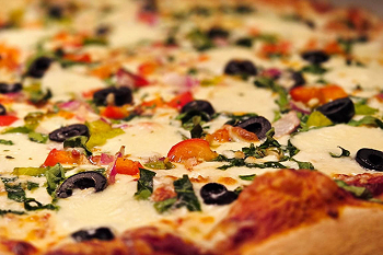 A close up of pizza topped with olives, tomatoes, onions and basil.